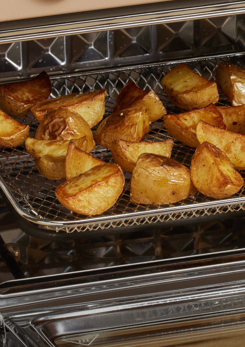 Quartered potatoes roasting on a mesh tray inside an oven, with golden-brown crispy edges visible.