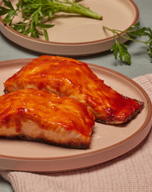 Two pieces of glazed salmon on a pink plate with green garnish.