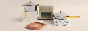 Set of cookware including pots, pans, and a small oven on a beige background