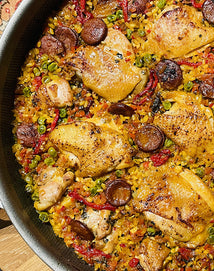 Paella with chicken, sausages, and vegetables in a pan on a wooden surface