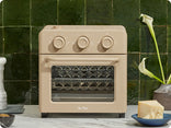 Beige toaster oven on a kitchen counter with a green tiled wall background