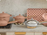 Set of cookware including pots and pans on a kitchen counter with a checkered backsplash.