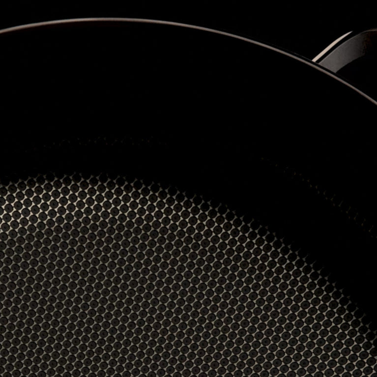 Close-up of a nonstick frying pan with a textured, honeycomb-patterned cooking surface against a dark background.