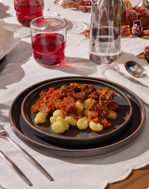 Dinner table setting with pasta dish, red wine, and water.