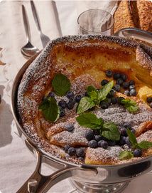 Dutch baby pancake with blueberries and mint leaves in a pan on a table.