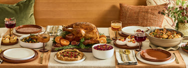 Dining table set for a meal with roasted turkey, sides, and drinks.