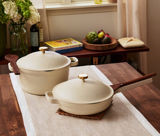 Two ceramic pots with wooden handles on a wooden table with a soft focus background.