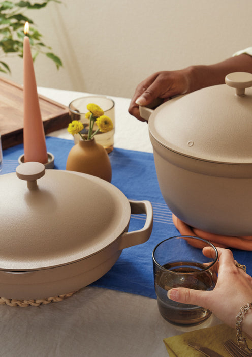Two ceramic pots on a table with a person holding a glass of water.
