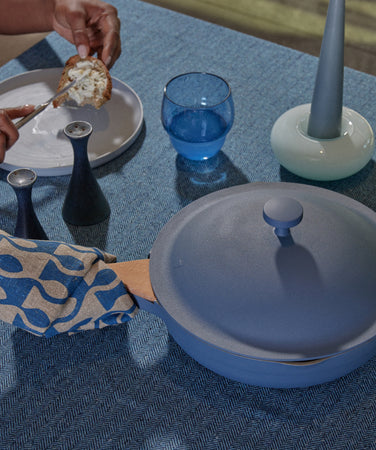 Person holding a pot with a blue lid on a table with various items