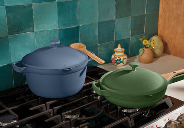 A blue Dutch oven and a green skillet with lids and wooden handles sit on a gas stovetop in a kitchen with teal tile backsplash.
