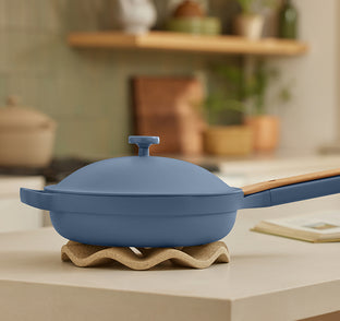 Blue frying pan with wooden handle on a wavy stand in a kitchen setting