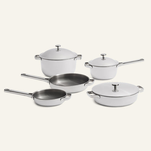A Titanium Pro Cookware Set + Braiser Pro consisting of five white stainless steel pots and pans with lids and handles.