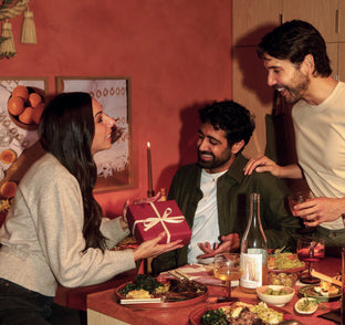 People gathered around a table with food and drinks, one person is giving a gift.