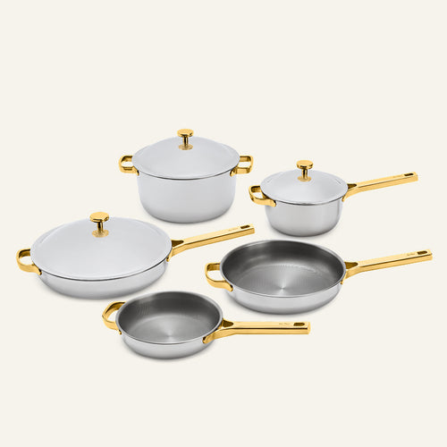 Titanium Pro Cookware Set+ featuring five stainless steel pieces with gold-toned handles and lids, including two lidded pots, two frying pans, and a deep skillet.
