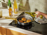 Person cooking food in a pan on a stove with bottles in the background