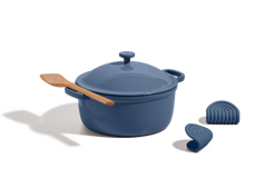 A blue Dutch oven with lid, a wooden spatula resting on top, and two blue silicone pot holders on a white background.
