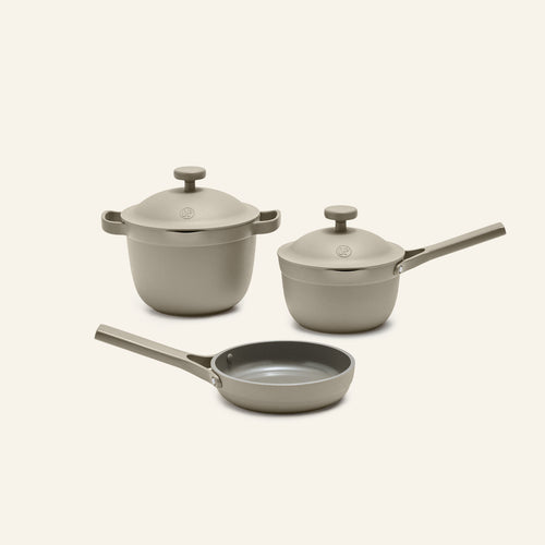 The Tiny Cookware Duo + Petite Perfect Pot, featuring a beige pot with lid, saucepan with lid, and skillet, is displayed on a light background.