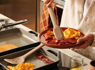 Person holding a plate of breakfast food with scrambled eggs and ham, next to a glass of orange juice.